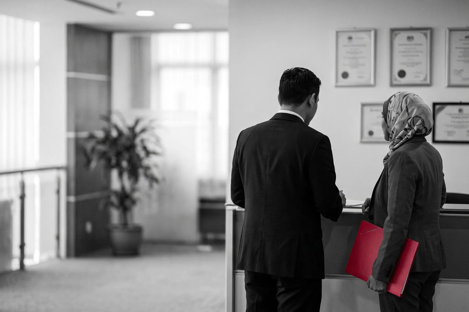Two visitors seen from behind at an office reception with framed certificates on the wall