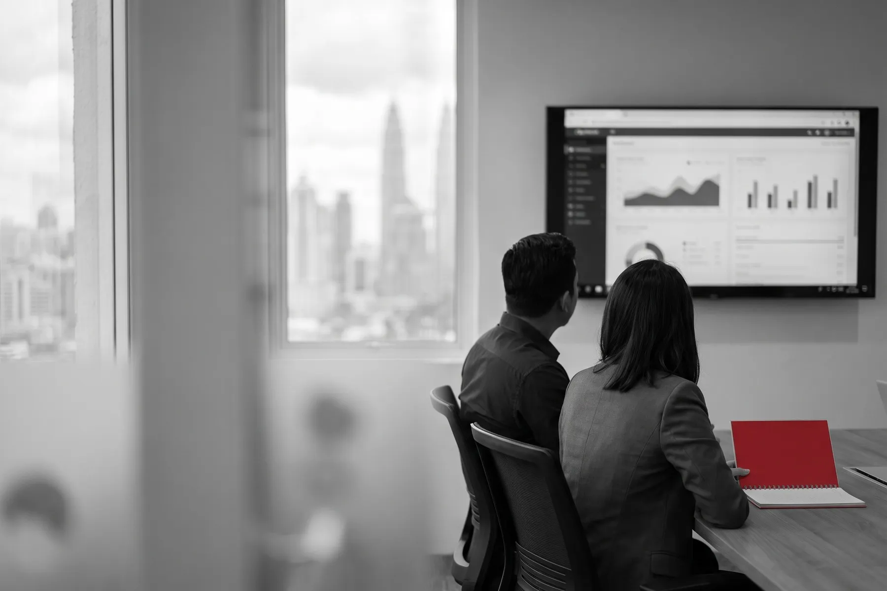 Two people seen from behind reviewing a cloud dashboard in a meeting room overlooking the city
